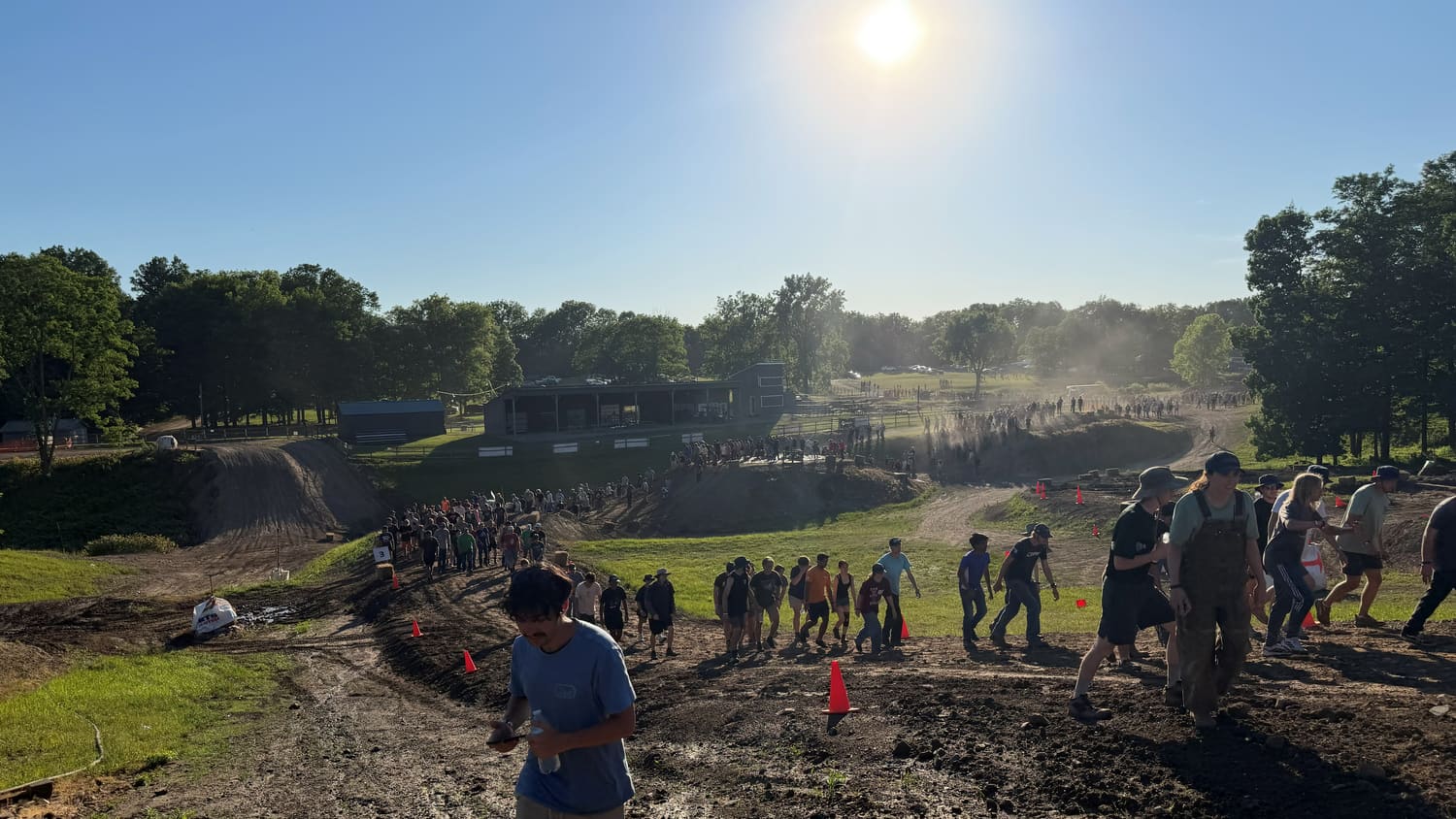 Teams walking the course past the rough terrain with the crowd spread along the bank